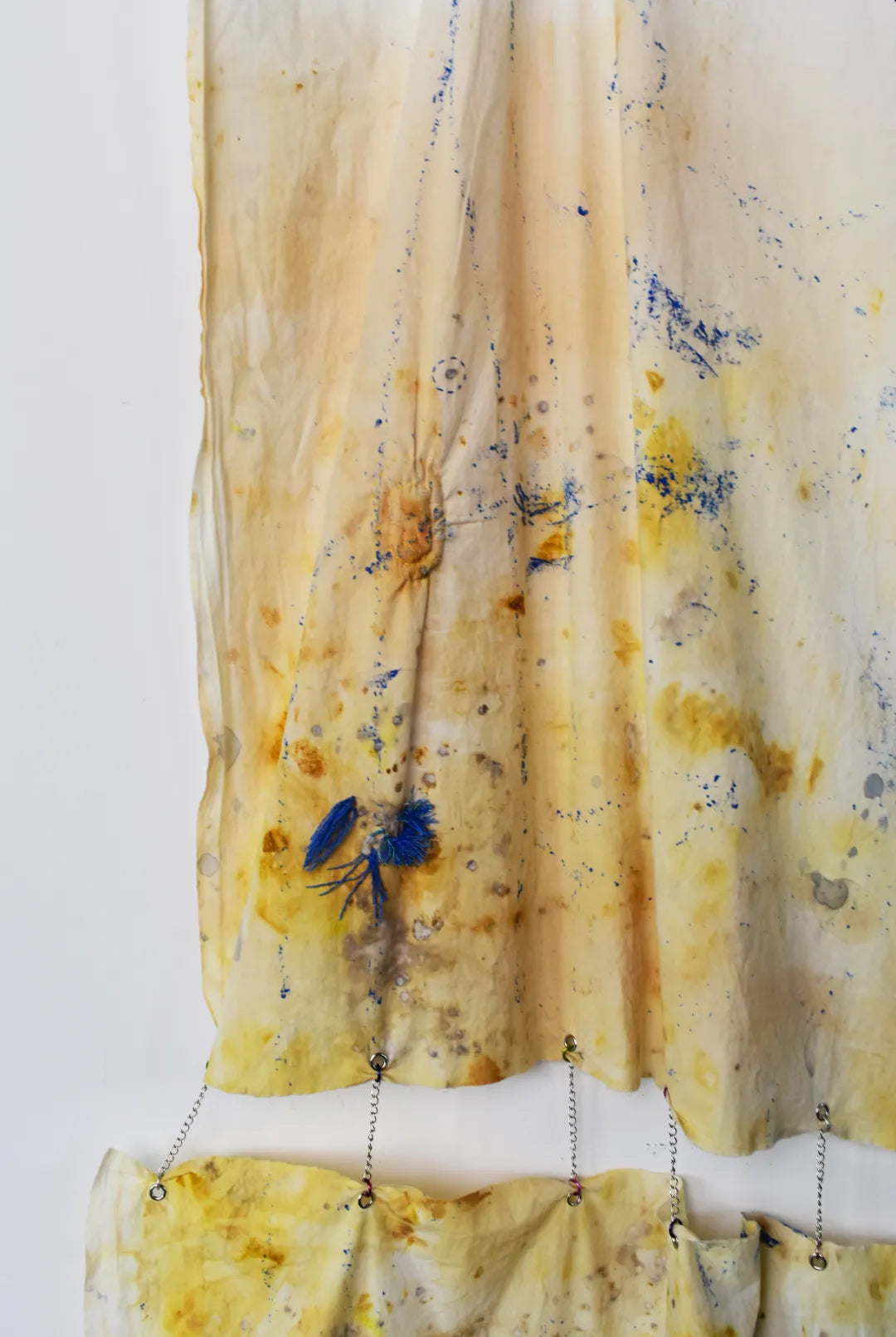 Close up of two pieces of fabric dyed with yellow and blue splattered ink, chained together with springs.