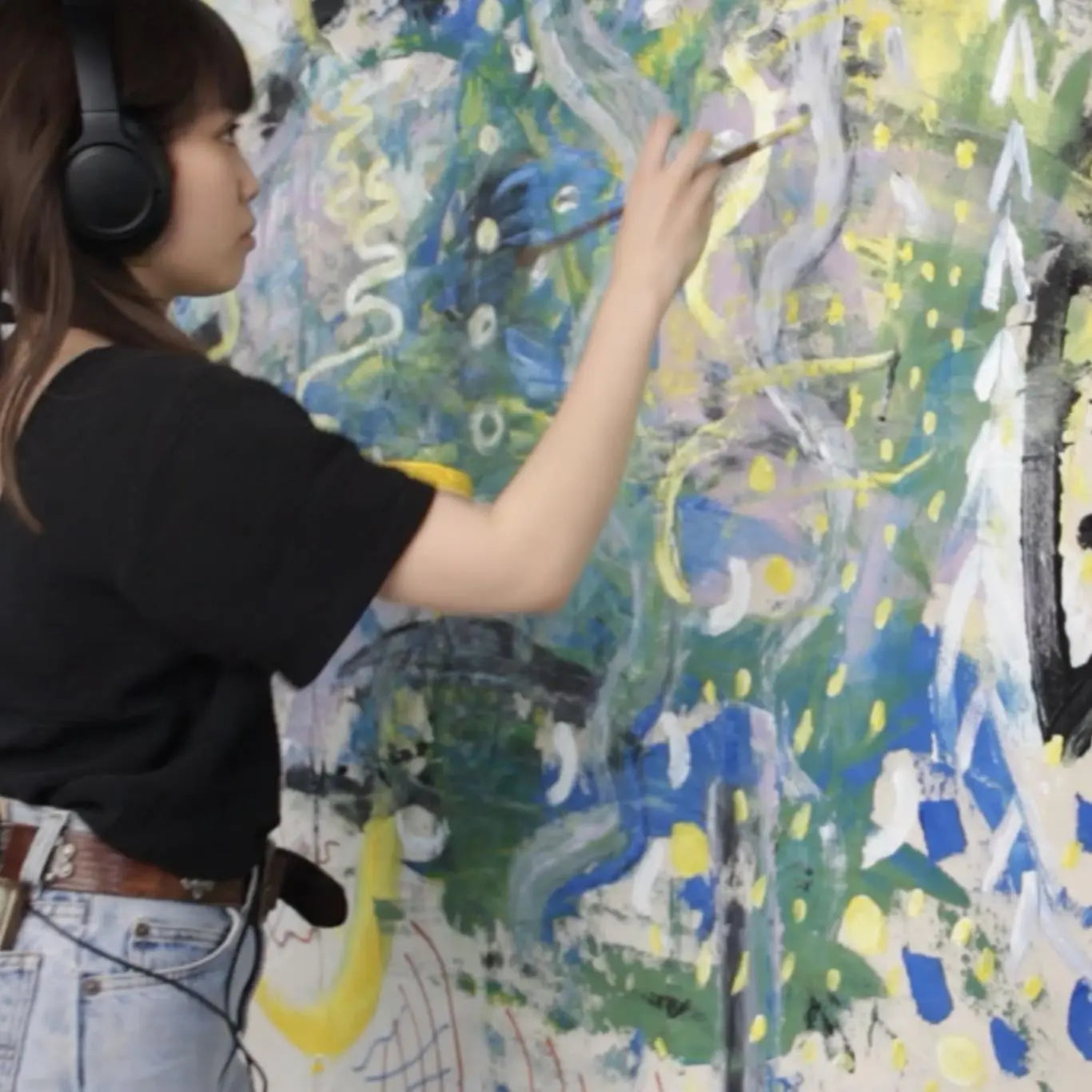 Person with headphones on, painting a large abstract painting.