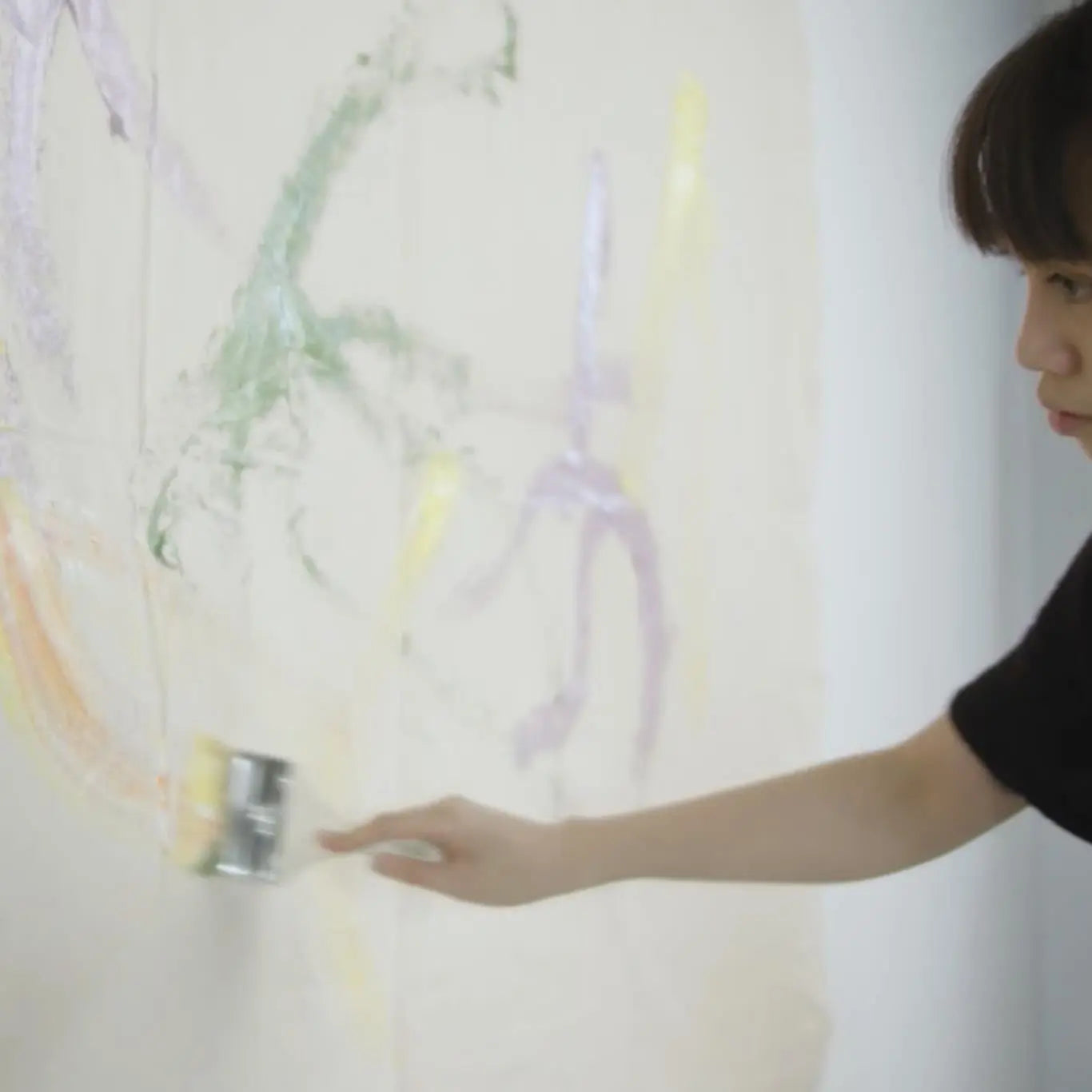 Person uses a large paintbrush to make an abstract line on a large canvas.