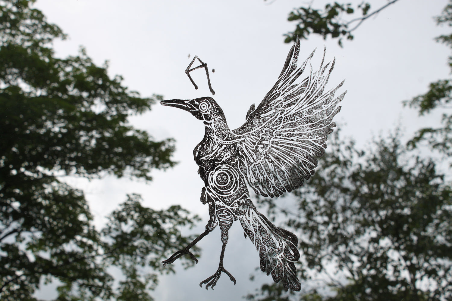 Printed bird on glass, facing to the left, with trees in the background.