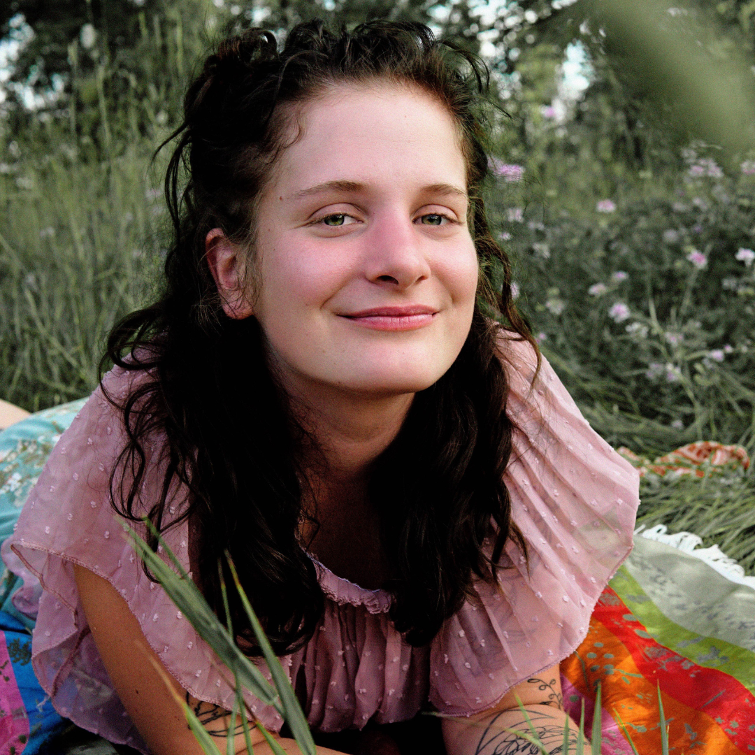 Person lying on a blanket in the grass, smiles at the camera.