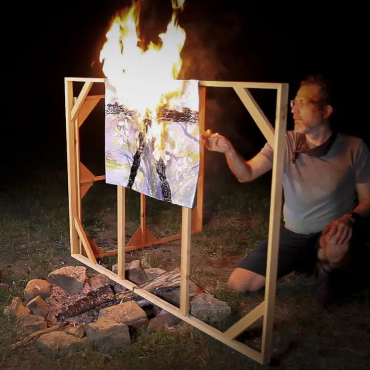 Person lights fire to a painted canvas over a campfire.