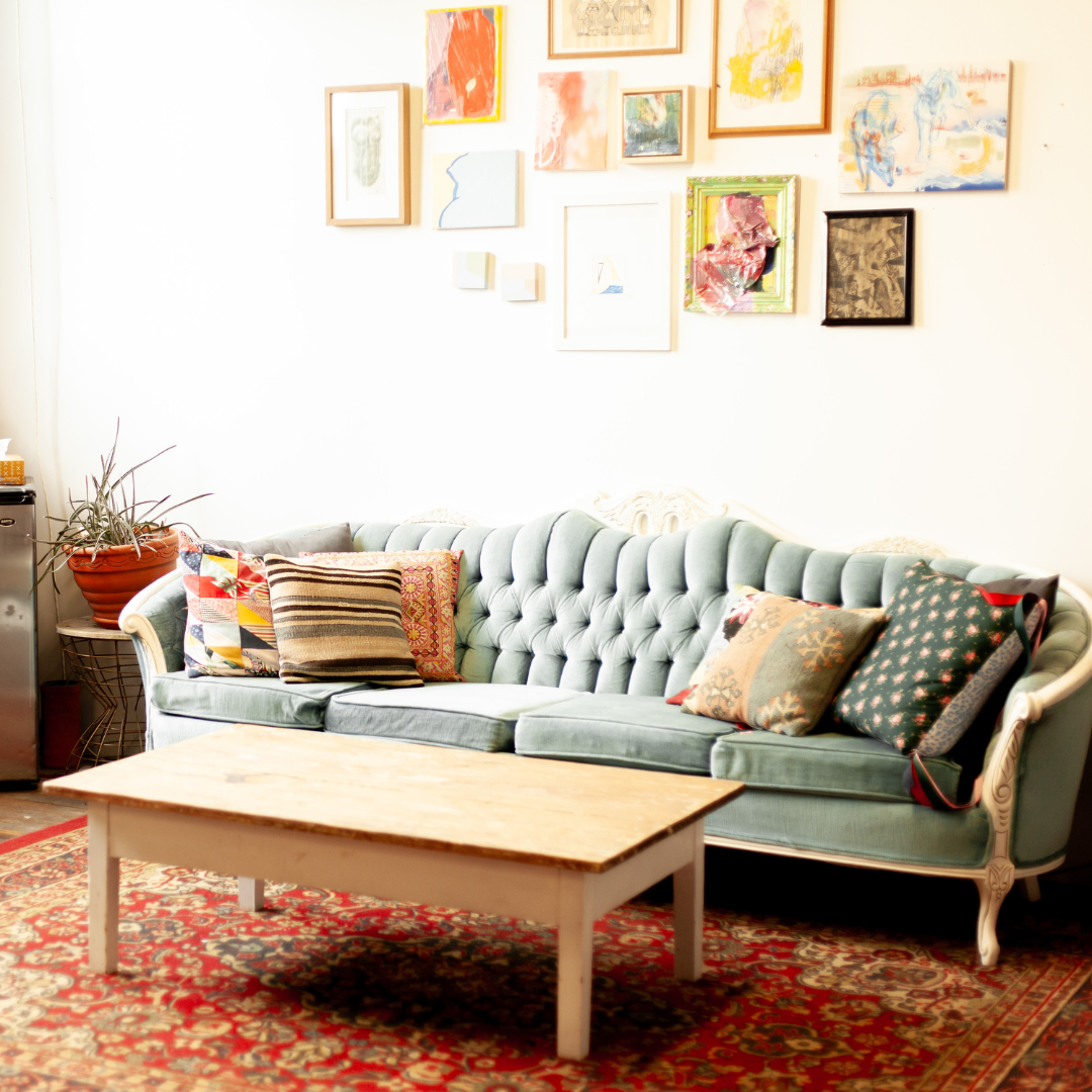 Vintage turquoise couch with colourful pillows sits against a white wall with salon-style hung artwork.