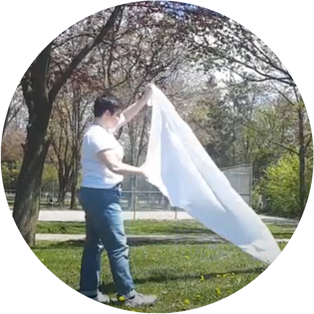 Circular image of a person holding a sheet blowing in the wind outside.