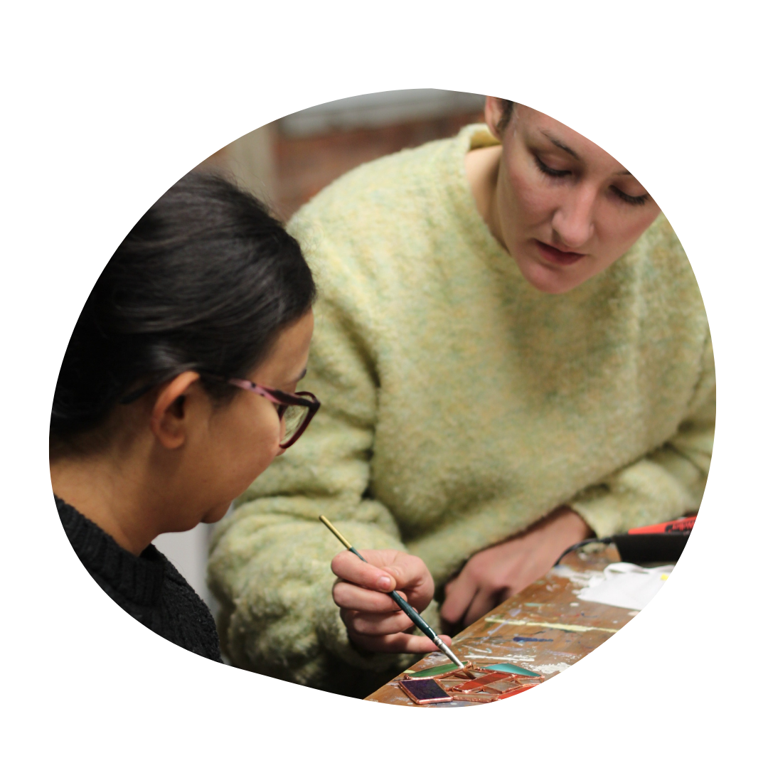 Person wearing a green sweater helps another person with a stained glass piece.