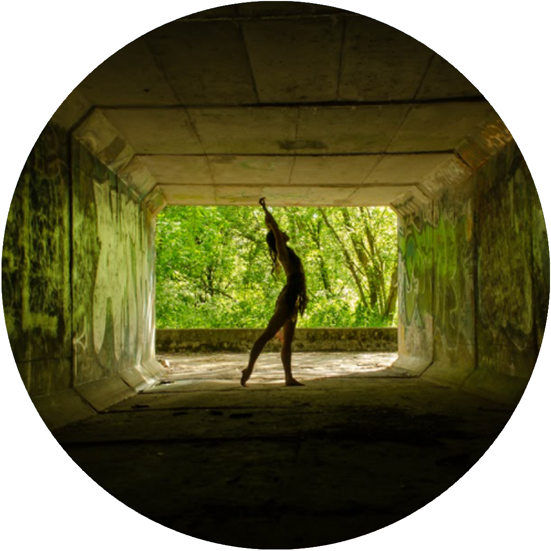 Circular image of a dancer holding a pose in a dark tunnel, backlit by greenery.